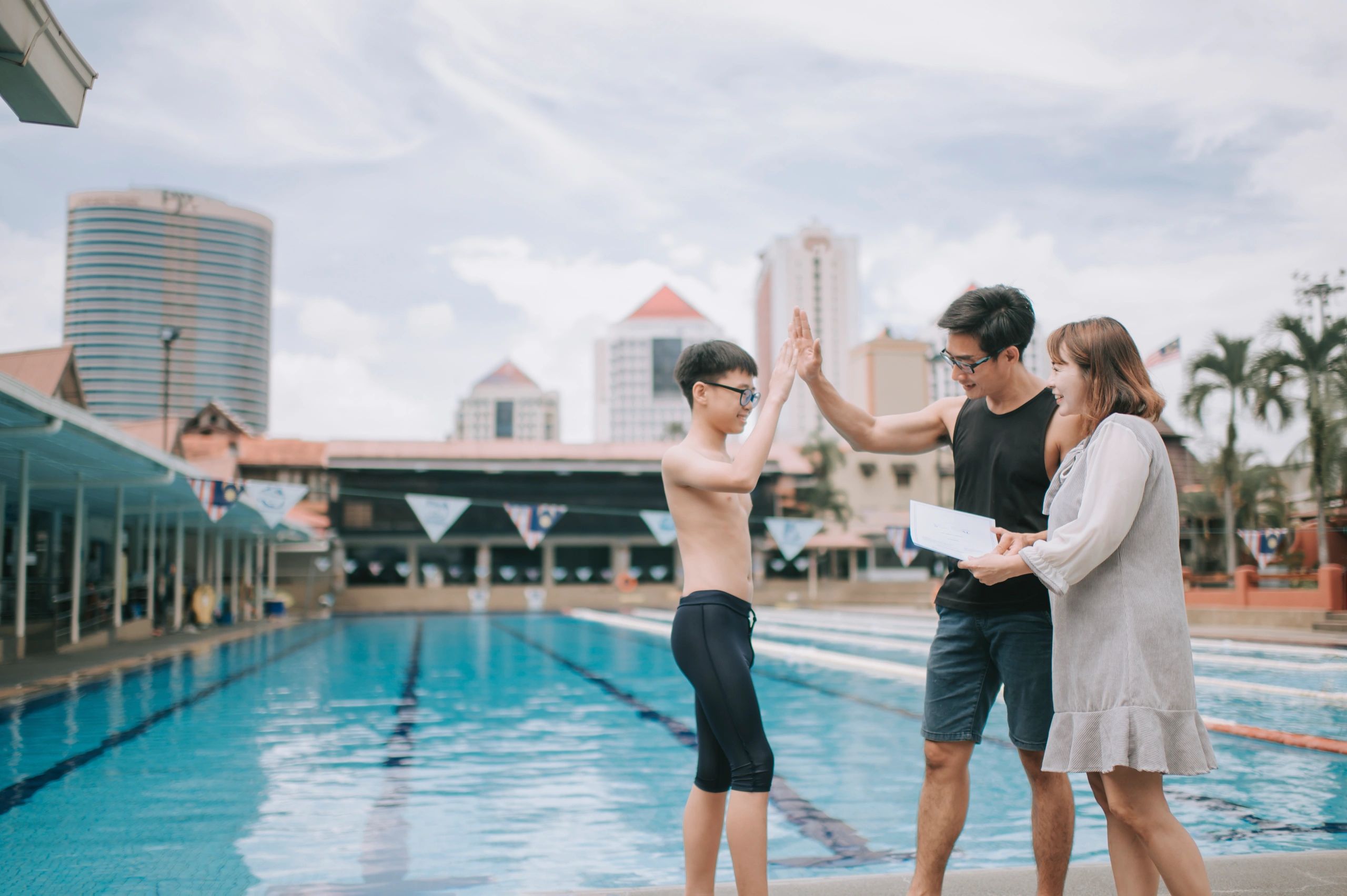 asian chinese parent give high five to their son proud of his swimming training class results at poolside