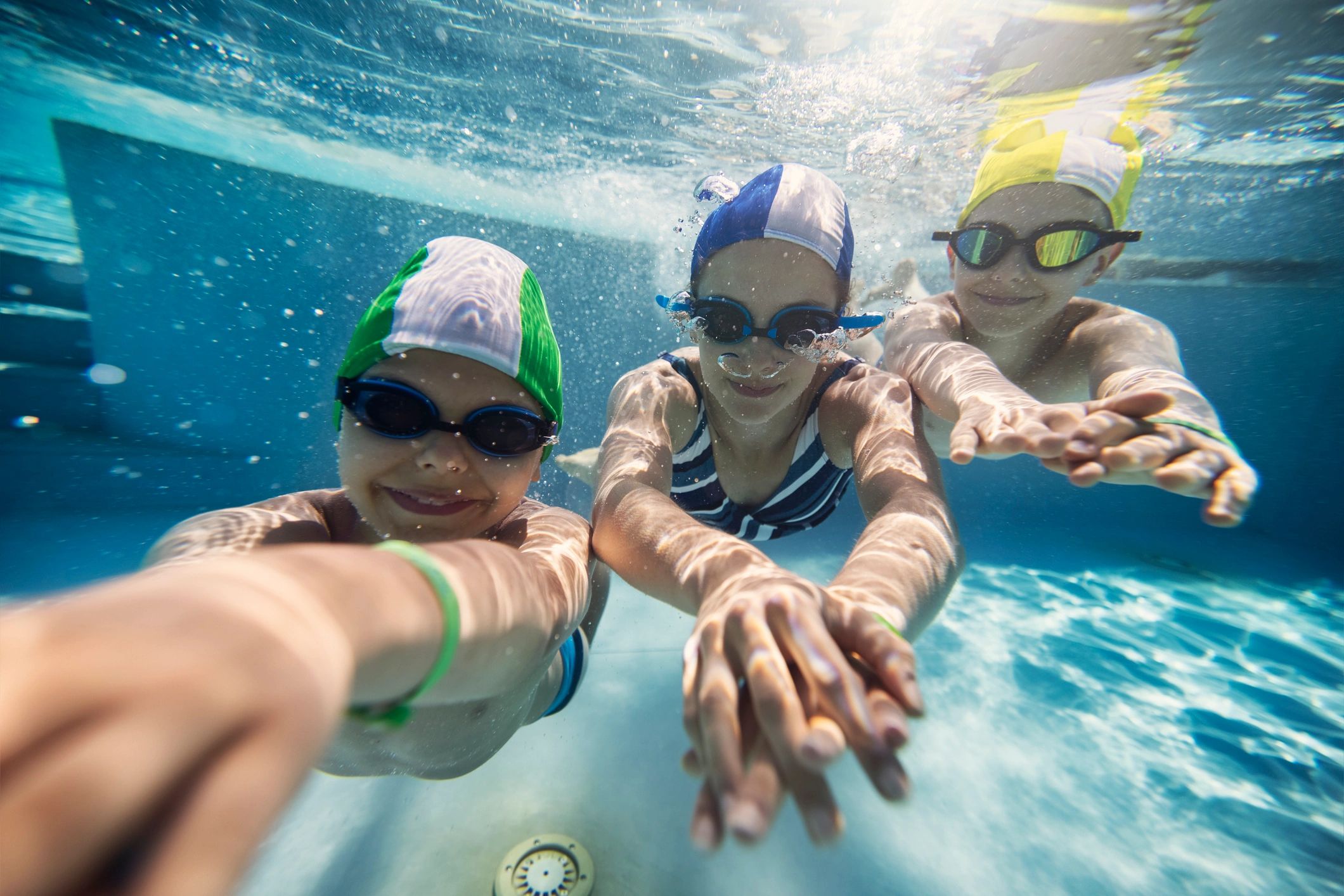 Three happy kids swimming underwater in pool